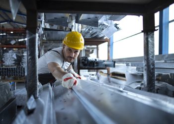 Factory worker working in warehouse handling metal material for production.