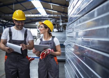 Factory workers walking in industrial plant and discussing about production efficiency.