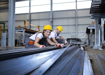 Industrial workers working in factory hall with metal.