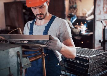 Portrait of a young worker in a hard hat at a large waste recycling factory. The engineer monitors the work of machines and other equipment.